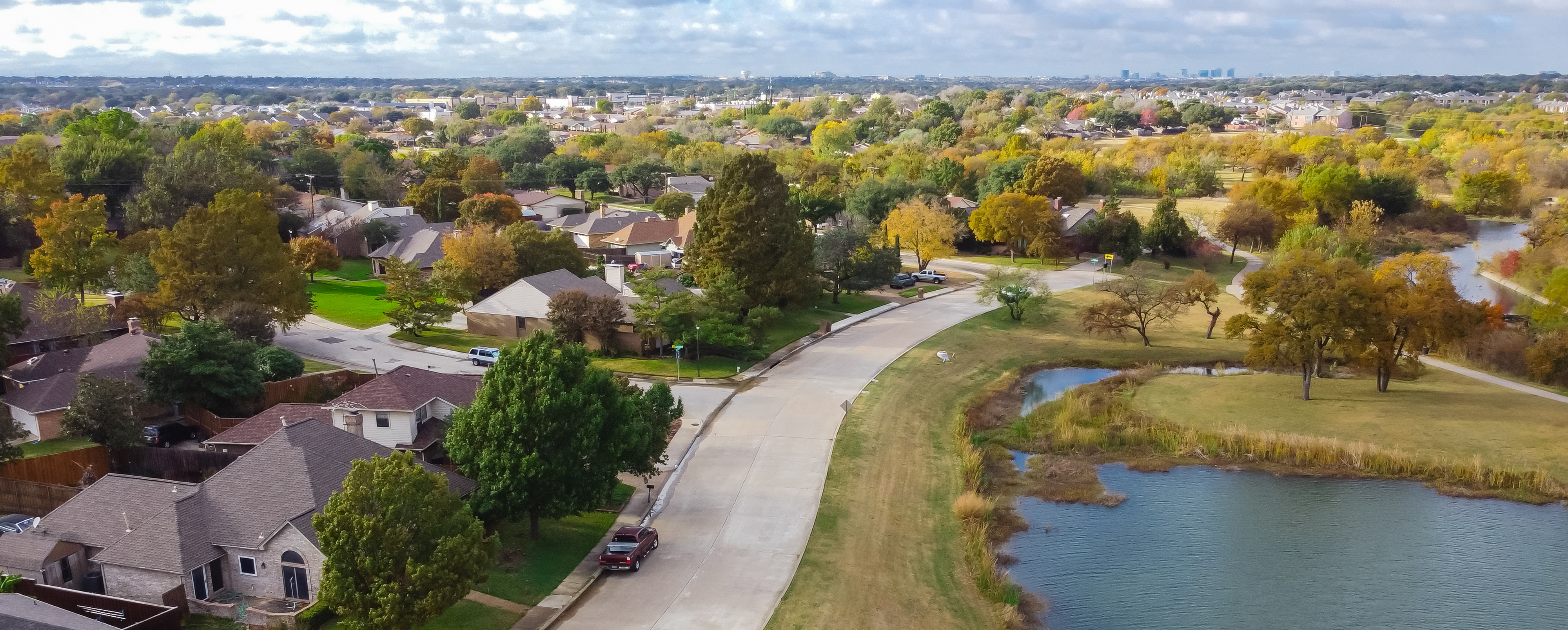 Aerial view lakeside and Parkside residential neighborhood downtown Dallas in distance background. Typical single family houses with matured trees bright fall foliages in Carrollton, Texas
