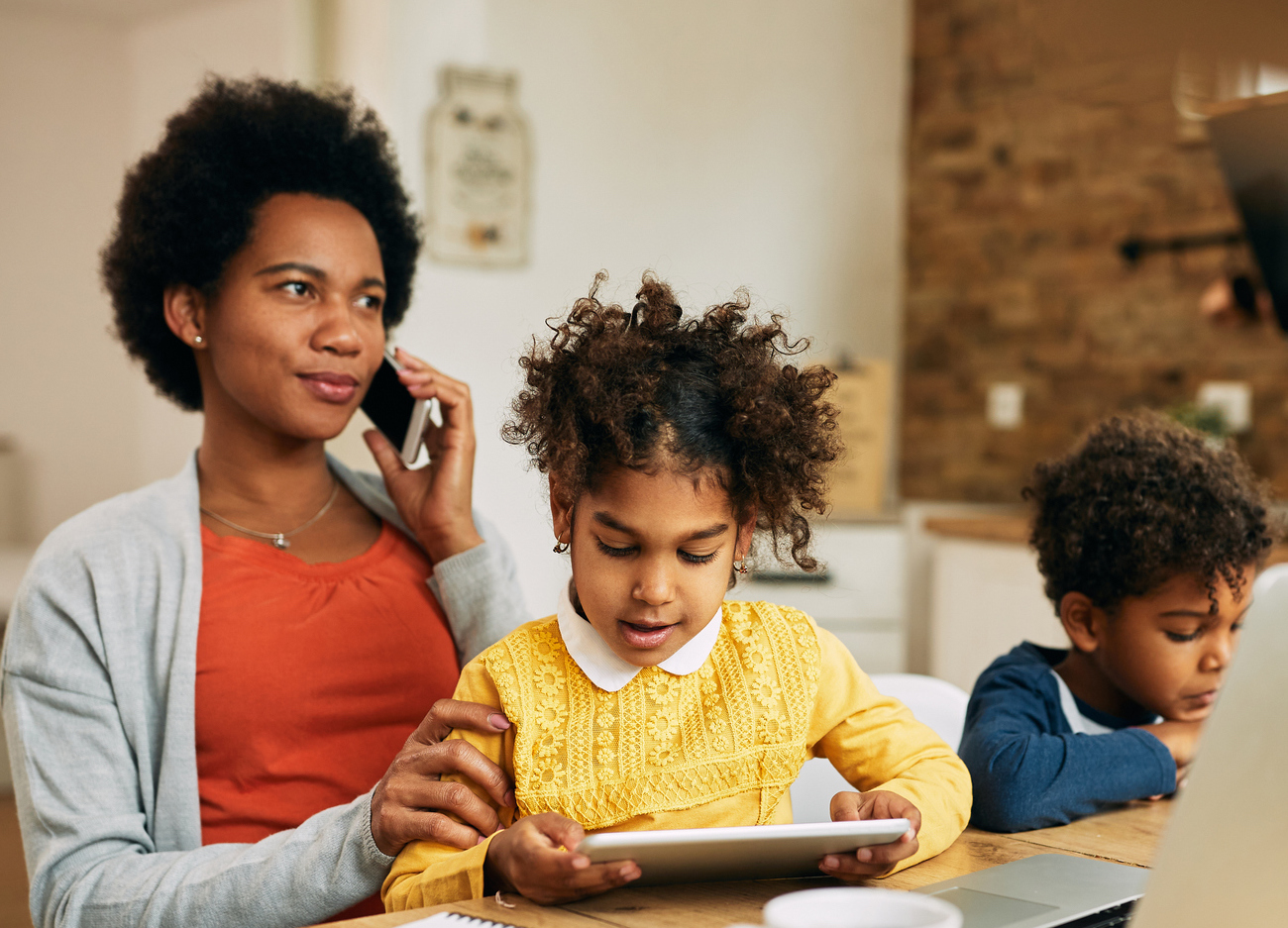 Working black mother with two children talking on cell phone at home.